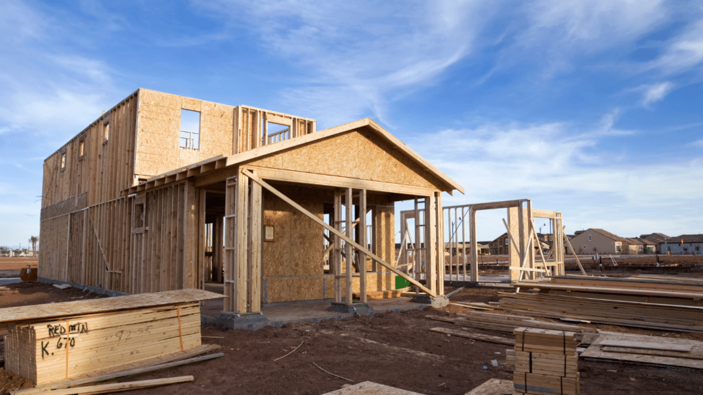 A wooden house frame under construction stands on a dirt lot, with building materials and other homes visible in the background under a blue sky—expertly managed by a trusted West Seattle remodeling contractor.