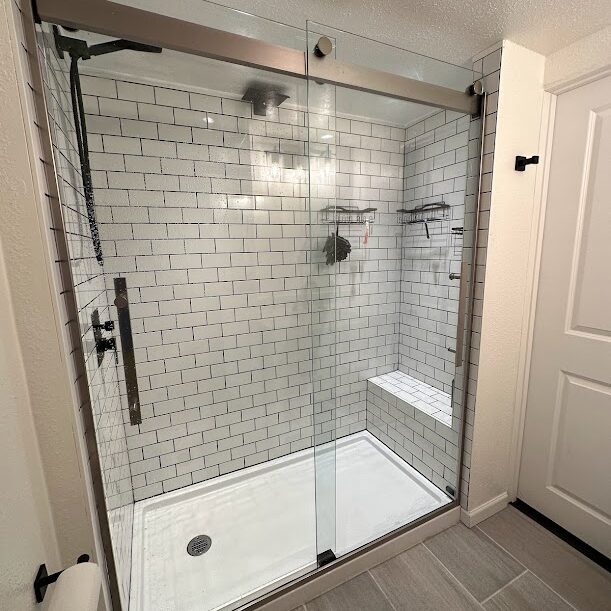 Modern shower with glass doors, white subway tile walls, built-in corner bench, black fixtures, and gray floor tiles—expertly crafted by a trusted West Seattle remodeling contractor.