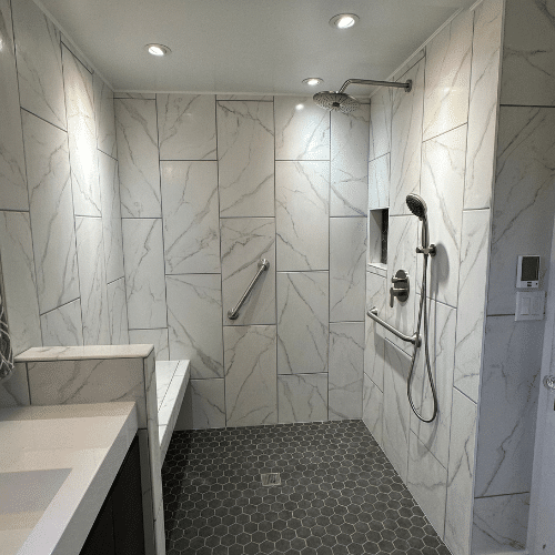 Modern walk-in shower with marble tile walls, hexagonal floor tiles, built-in bench, grab bar, overhead and handheld showerheads, and a recessed shelf—expertly designed by a top West Seattle remodeling contractor.