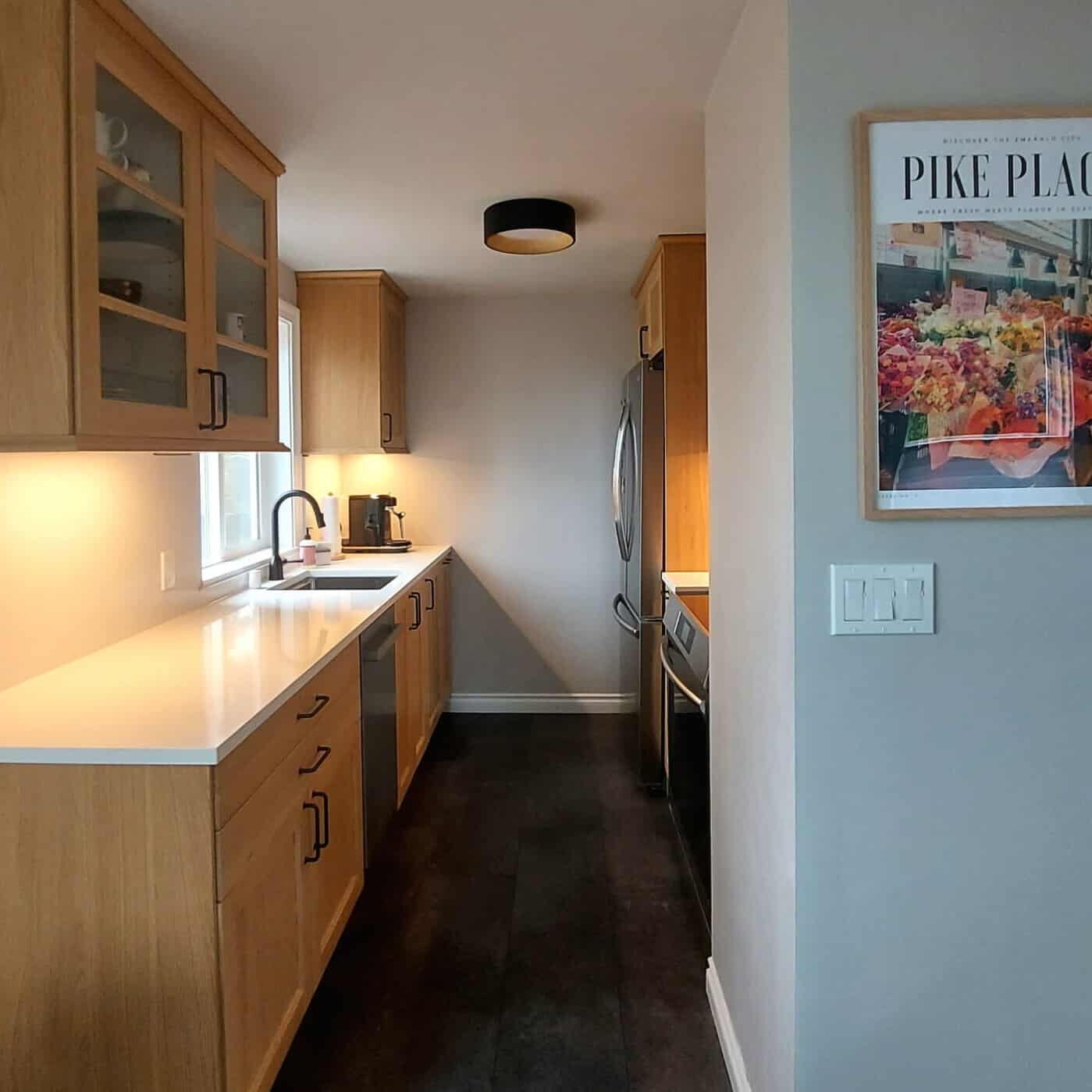 A modern galley kitchen with wood cabinets, white countertops, and a Pike Place market poster on the wall—expertly crafted by a West Seattle remodeling contractor.
